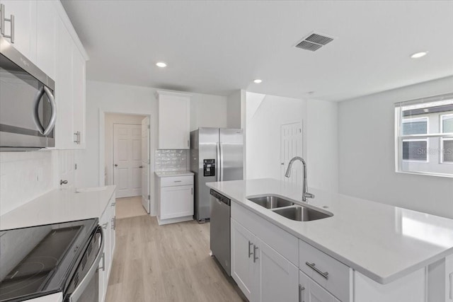 kitchen featuring white cabinets, light hardwood / wood-style flooring, appliances with stainless steel finishes, sink, and a center island with sink