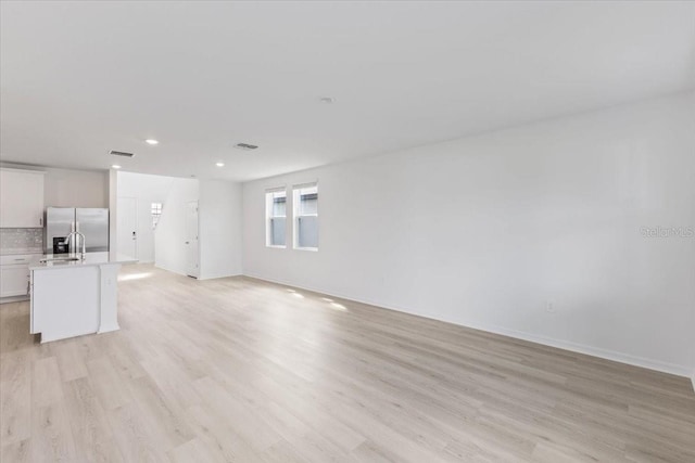 unfurnished living room featuring sink and light hardwood / wood-style floors