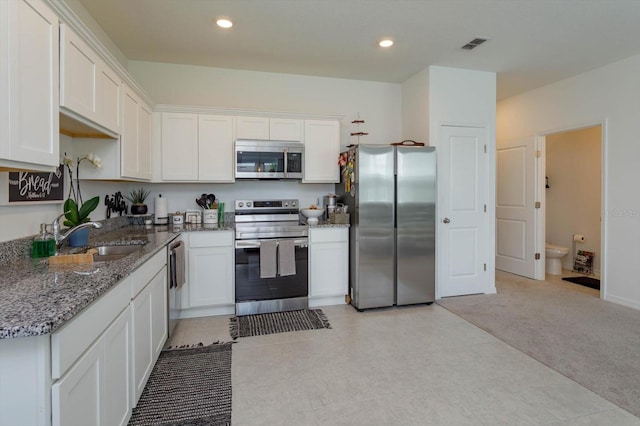 kitchen with dark stone counters, white cabinets, sink, light tile patterned flooring, and stainless steel appliances