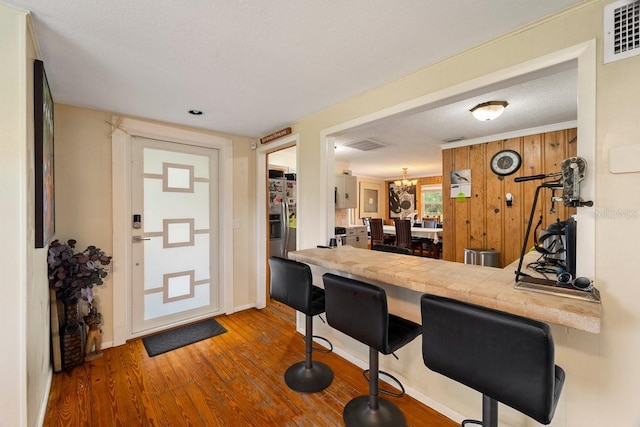 kitchen with stainless steel fridge with ice dispenser, a kitchen bar, hardwood / wood-style flooring, kitchen peninsula, and a textured ceiling