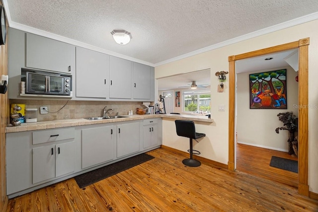 kitchen featuring sink, ornamental molding, light hardwood / wood-style floors, tasteful backsplash, and ceiling fan