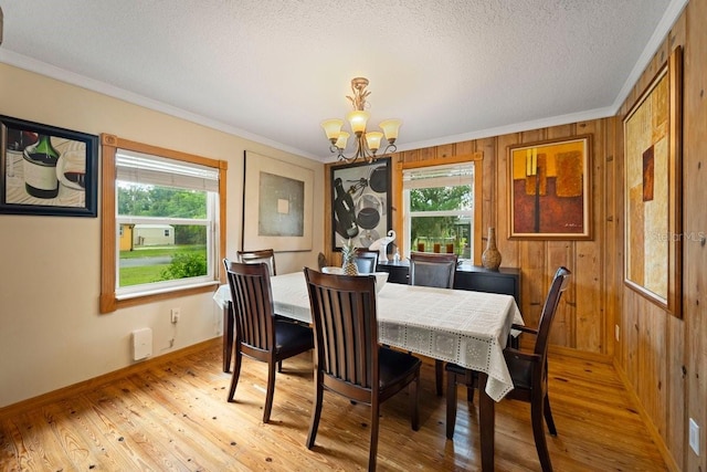 dining space with light wood-type flooring, wood walls, a notable chandelier, and crown molding