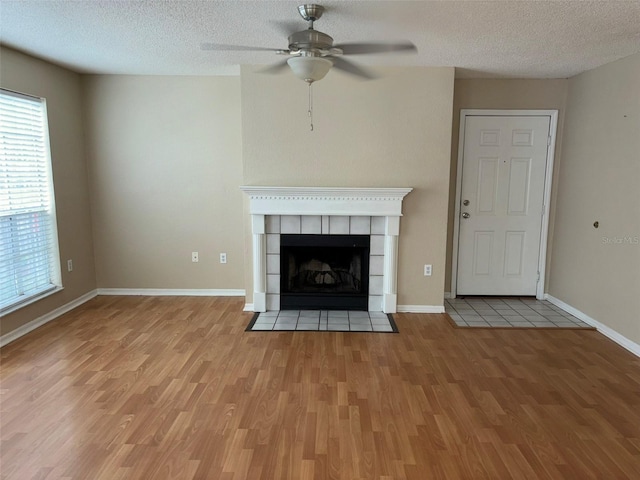 unfurnished living room with ceiling fan, light hardwood / wood-style floors, a textured ceiling, and a tiled fireplace