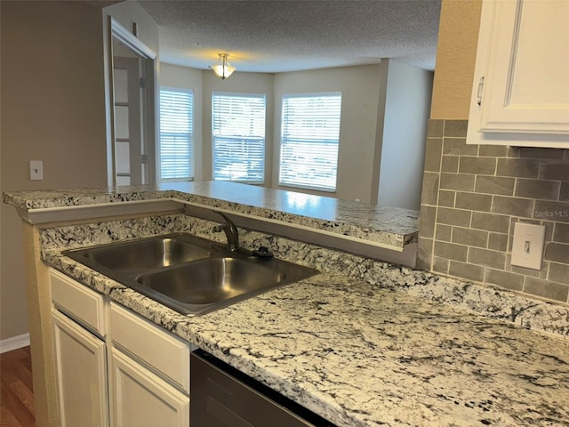 kitchen featuring sink, hardwood / wood-style flooring, light stone countertops, a textured ceiling, and white cabinetry