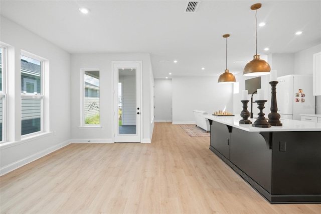 kitchen with light hardwood / wood-style flooring, hanging light fixtures, white fridge, and a breakfast bar