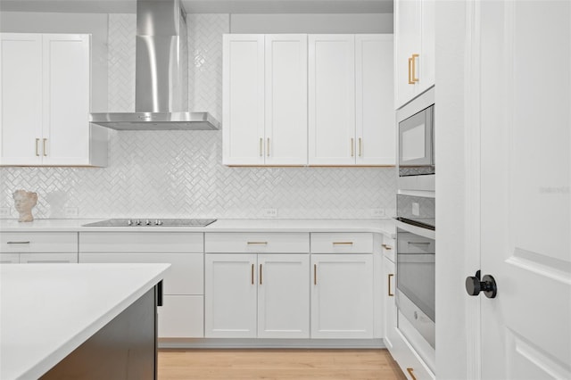 kitchen featuring light hardwood / wood-style flooring, wall chimney range hood, stainless steel appliances, and white cabinetry