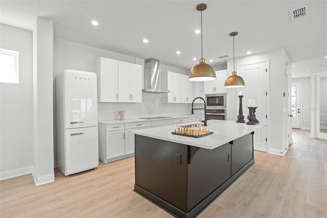 kitchen with light hardwood / wood-style flooring, white cabinetry, appliances with stainless steel finishes, wall chimney exhaust hood, and a center island with sink