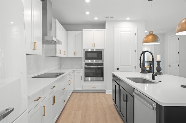 kitchen with stainless steel appliances, sink, light hardwood / wood-style floors, decorative light fixtures, and wall chimney range hood