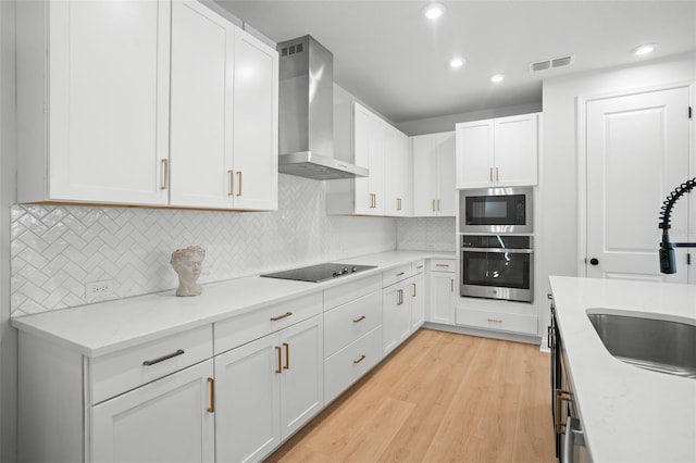 kitchen featuring white cabinetry, oven, light hardwood / wood-style flooring, wall chimney range hood, and built in microwave