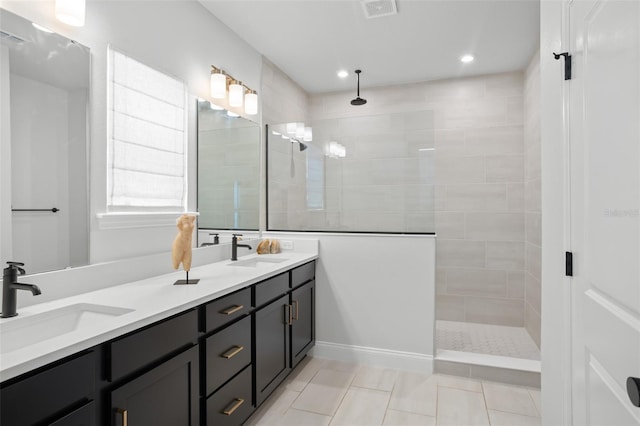 bathroom with dual bowl vanity, a tile shower, and tile patterned flooring