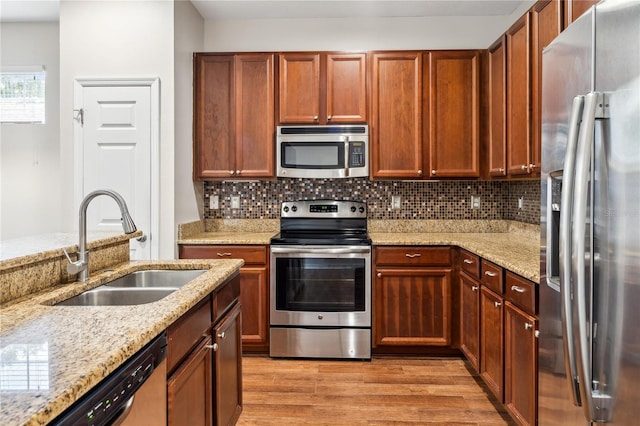 kitchen with stainless steel appliances, light wood-type flooring, backsplash, sink, and light stone counters