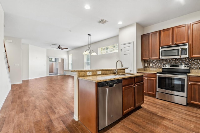 kitchen with an island with sink, sink, stainless steel appliances, and hardwood / wood-style flooring