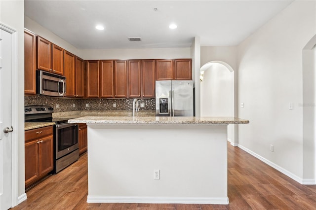 kitchen with appliances with stainless steel finishes, backsplash, a center island with sink, and wood-type flooring