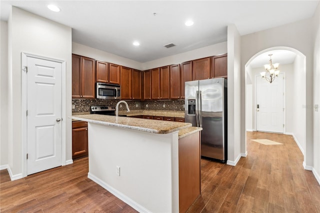 kitchen with appliances with stainless steel finishes, an island with sink, hardwood / wood-style flooring, and backsplash