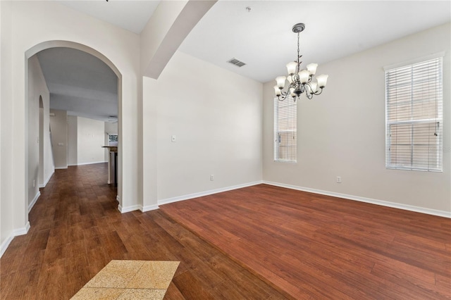 empty room with dark wood-type flooring and an inviting chandelier