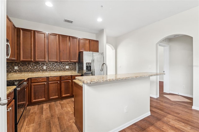 kitchen featuring appliances with stainless steel finishes, a center island with sink, light stone counters, and dark wood-type flooring