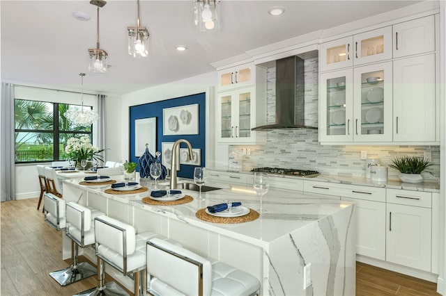 kitchen with sink, an island with sink, hanging light fixtures, and wall chimney range hood