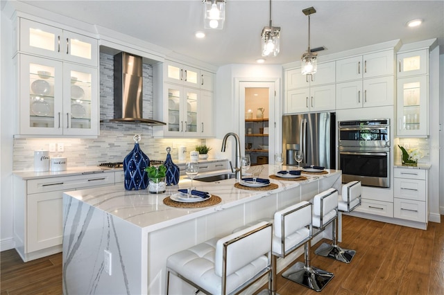 kitchen featuring appliances with stainless steel finishes, sink, a kitchen island with sink, wall chimney exhaust hood, and dark hardwood / wood-style flooring