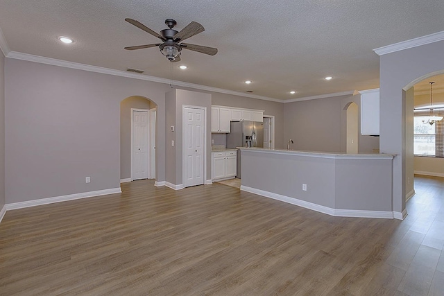 unfurnished living room with ceiling fan with notable chandelier, a textured ceiling, light wood-type flooring, and crown molding