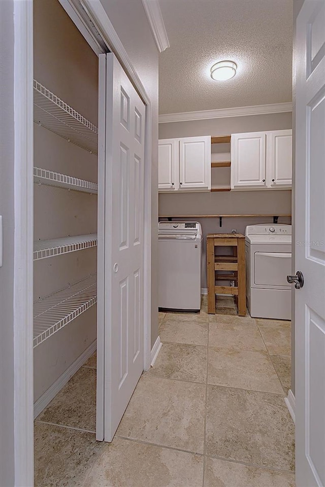 washroom with cabinets, ornamental molding, a textured ceiling, washer and clothes dryer, and light tile patterned floors