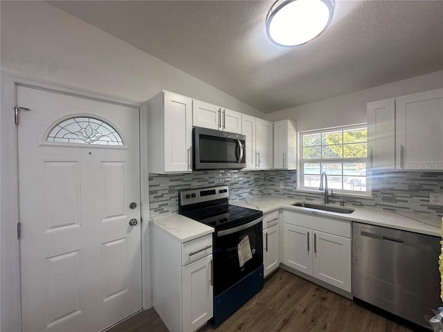 kitchen with white cabinetry, sink, stainless steel appliances, vaulted ceiling, and decorative backsplash