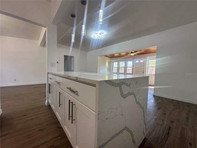 kitchen featuring dark wood-type flooring, hanging light fixtures, vaulted ceiling, light stone countertops, and white cabinetry