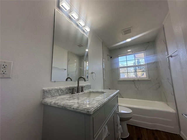 full bathroom featuring vanity, a textured ceiling, tiled shower / bath combo, hardwood / wood-style floors, and toilet