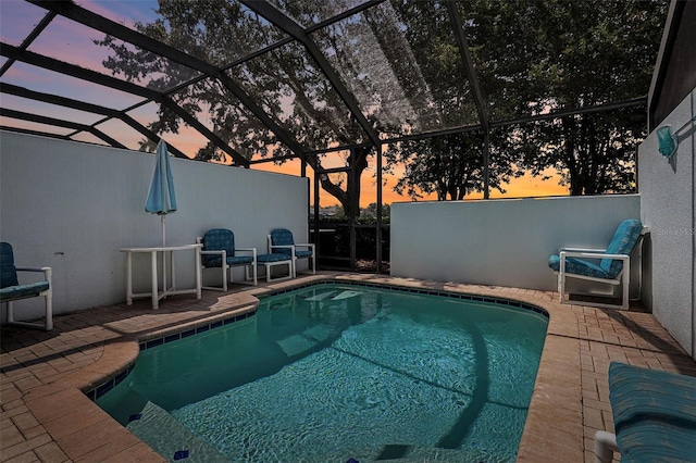 pool at dusk with glass enclosure and a patio area