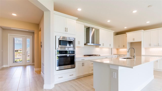 kitchen with white cabinets, a kitchen island with sink, wall chimney exhaust hood, and appliances with stainless steel finishes