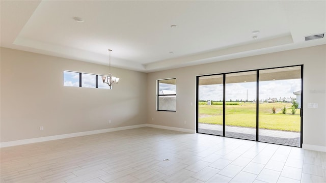 spare room with light hardwood / wood-style flooring, a tray ceiling, and an inviting chandelier