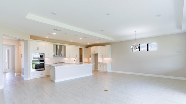 kitchen with sink, wall chimney exhaust hood, an island with sink, white cabinetry, and stainless steel appliances