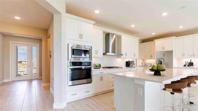 kitchen featuring stainless steel appliances, a center island with sink, white cabinetry, and wall chimney exhaust hood