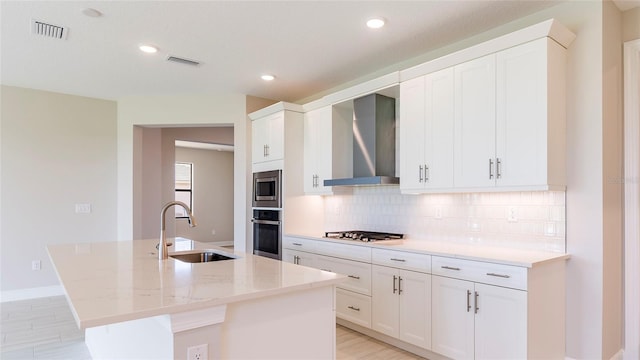 kitchen featuring a kitchen island with sink, sink, stainless steel appliances, and wall chimney range hood