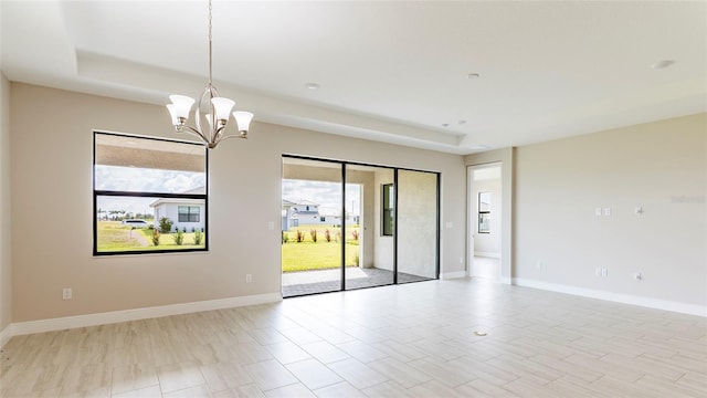 spare room with a tray ceiling, light wood-type flooring, and an inviting chandelier