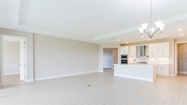 kitchen featuring stainless steel appliances, wall chimney range hood, decorative backsplash, a center island with sink, and white cabinets