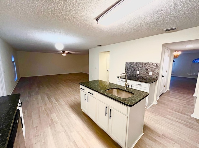 kitchen featuring ceiling fan, light wood-type flooring, decorative backsplash, a kitchen island with sink, and sink