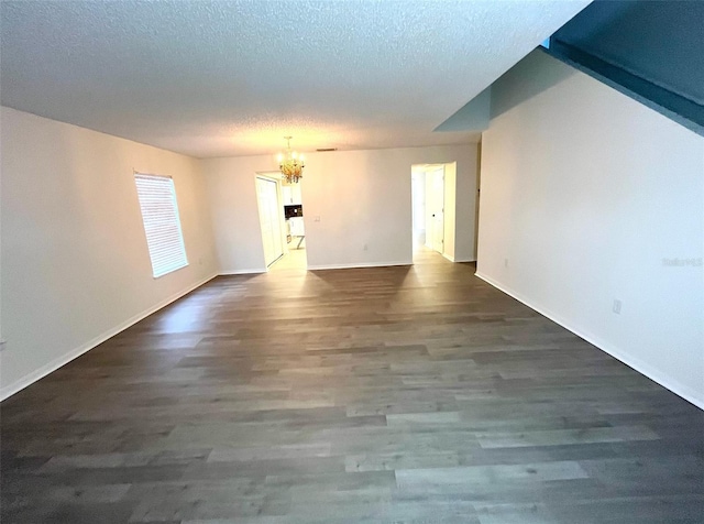 empty room with an inviting chandelier, wood finished floors, baseboards, and a textured ceiling