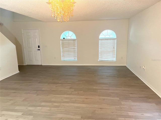 unfurnished room featuring an inviting chandelier, a textured ceiling, baseboards, and wood finished floors