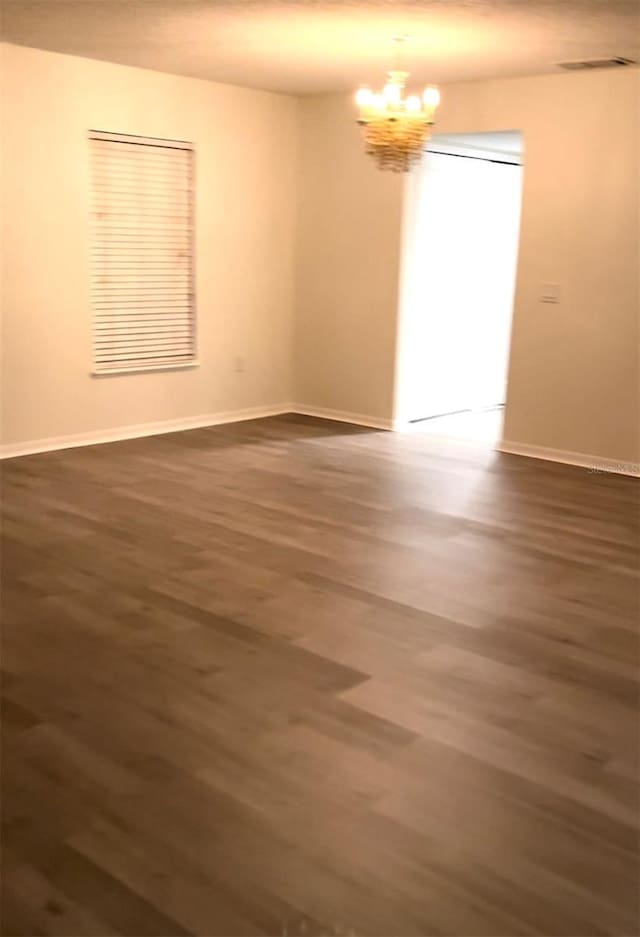 empty room with baseboards, visible vents, a chandelier, and dark wood finished floors