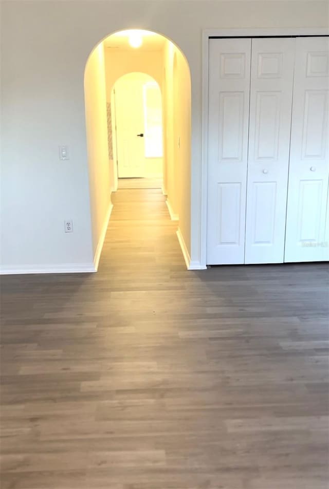 hallway featuring arched walkways, baseboards, and wood finished floors