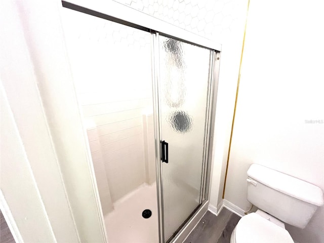 bathroom featuring toilet, wood finished floors, baseboards, and a shower stall