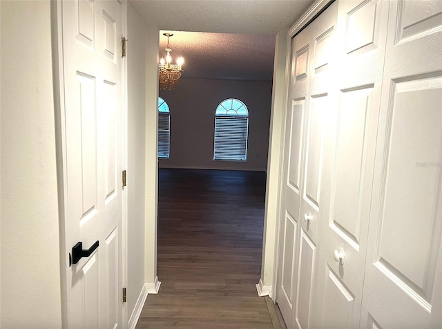 corridor with a textured ceiling, dark wood-type flooring, and an inviting chandelier