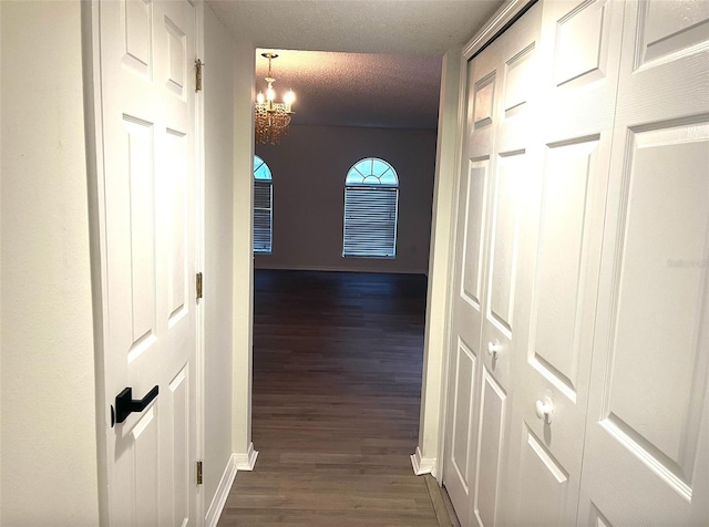hallway featuring baseboards, a notable chandelier, dark wood-type flooring, and a textured ceiling