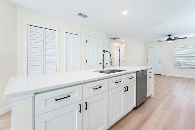 kitchen featuring a center island with sink, white cabinets, stainless steel dishwasher, sink, and light wood-type flooring