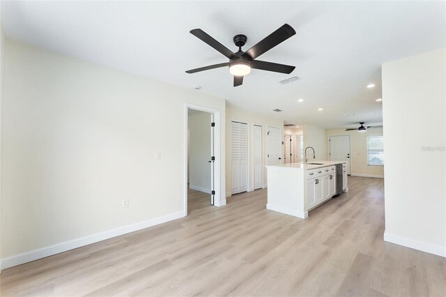 kitchen with light hardwood / wood-style flooring, an island with sink, sink, ceiling fan, and white cabinets