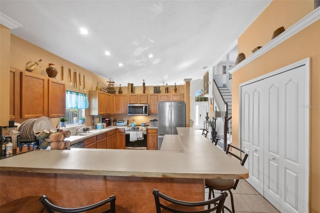 kitchen featuring stainless steel appliances, a kitchen bar, sink, kitchen peninsula, and light tile patterned flooring