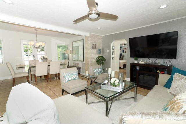 living room with light tile patterned floors, ceiling fan with notable chandelier, and brick wall