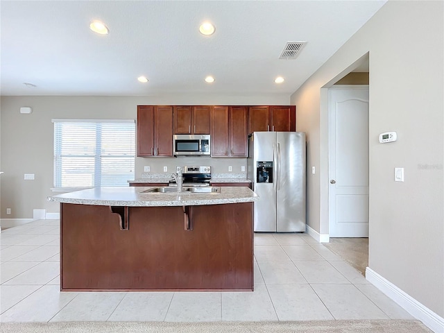 kitchen with light tile patterned floors, sink, stainless steel appliances, and a center island with sink