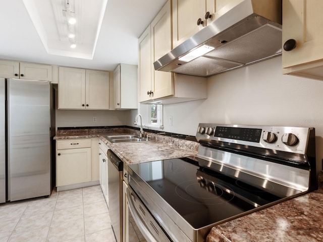 kitchen with stainless steel appliances, sink, a tray ceiling, light tile patterned flooring, and cream cabinetry