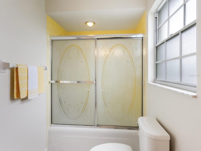 bathroom with toilet and bath / shower combo with glass door